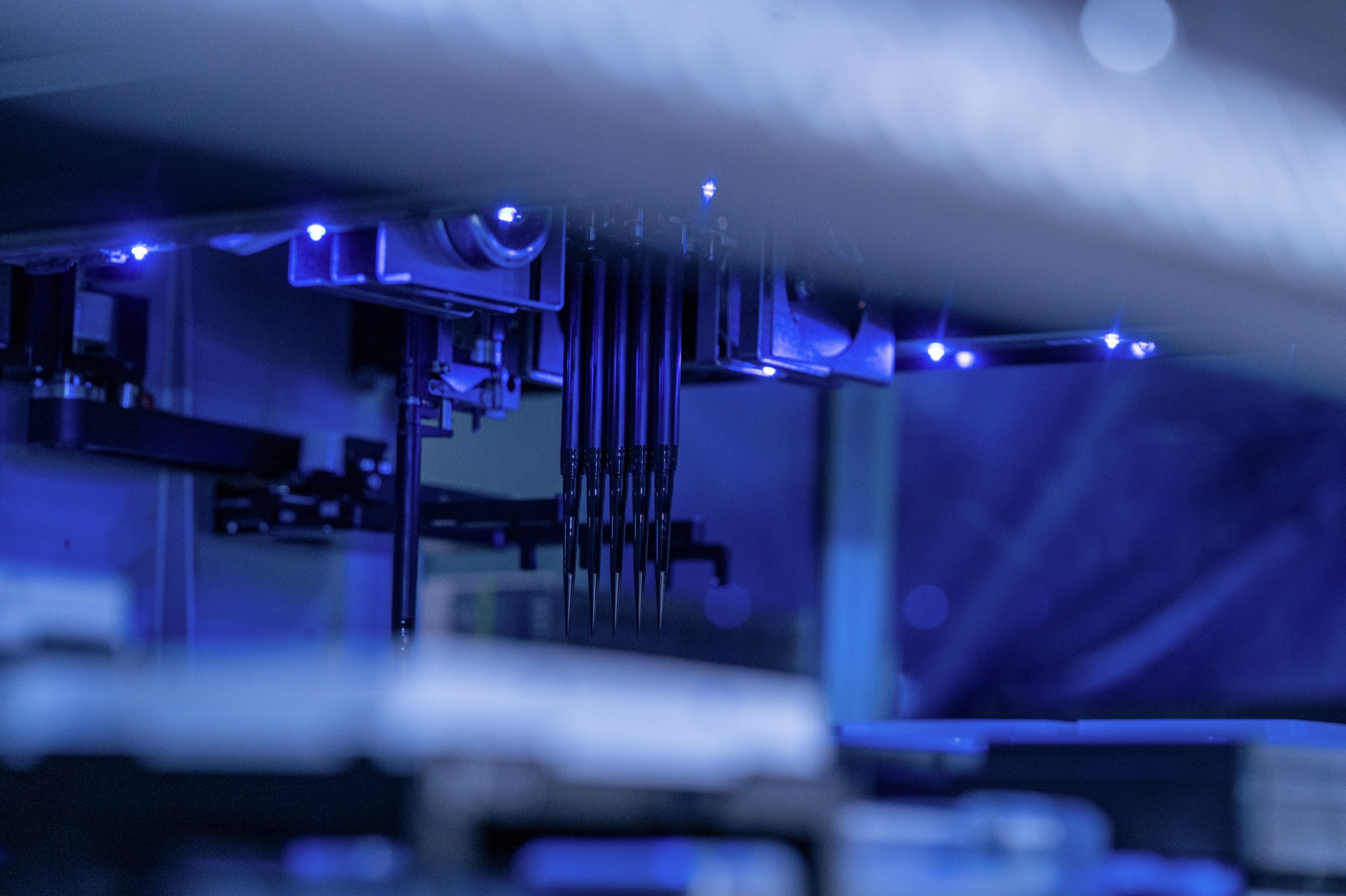 Automated laboratory liquid handling robot operating under blue UV light in research facility