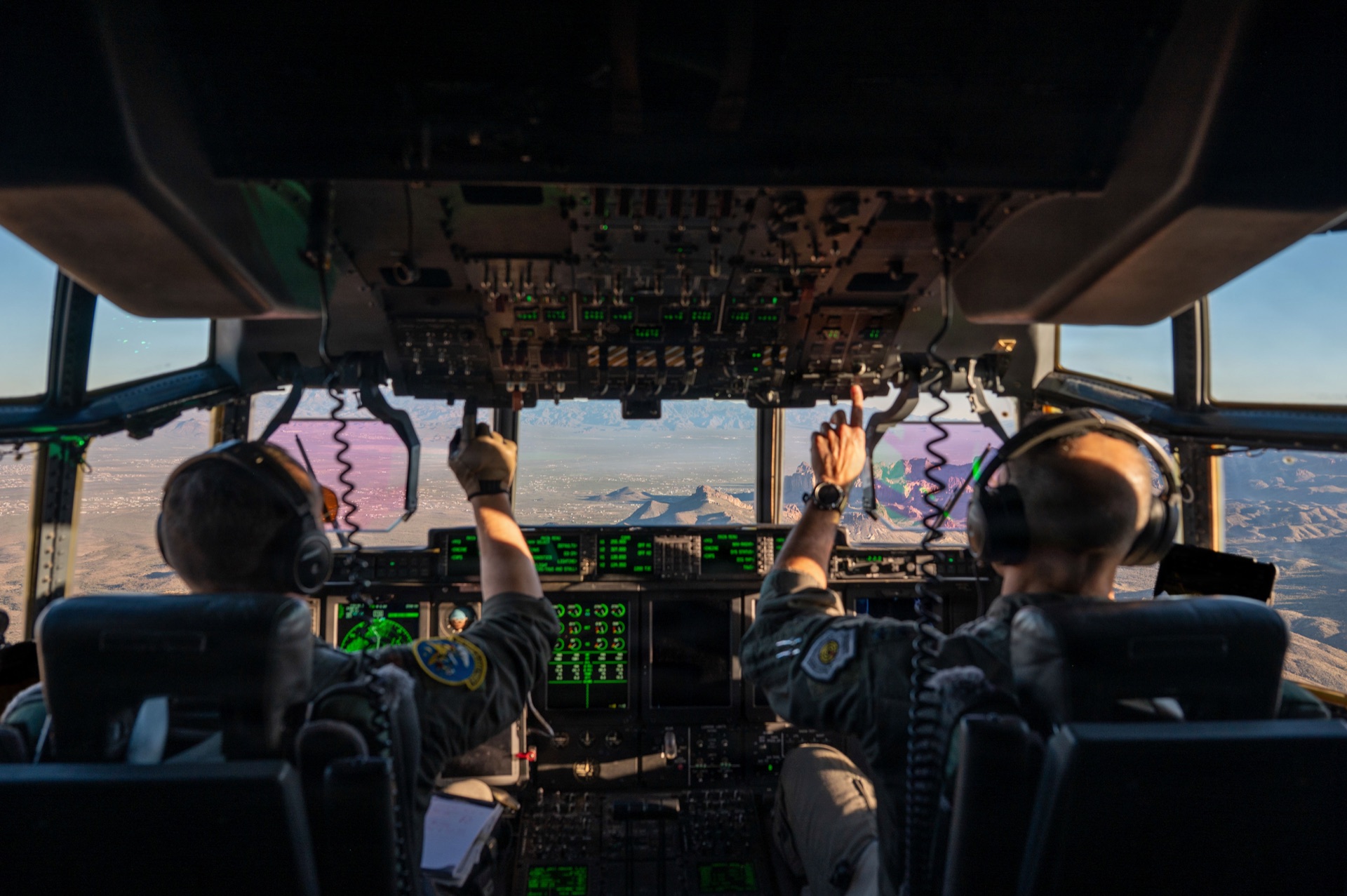 Military aircrew operating aircraft cockpit over mountain range during mission