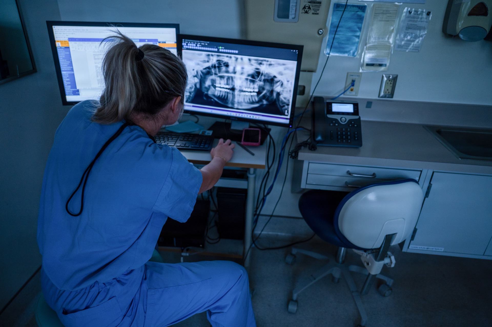 Healthcare professional reviewing patient dental X-rays on dual monitor workstation